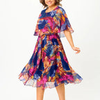 A flowing plus-size summer dress in a vibrant floral pattern with shades of blue and pink, featuring short sleeves. 0