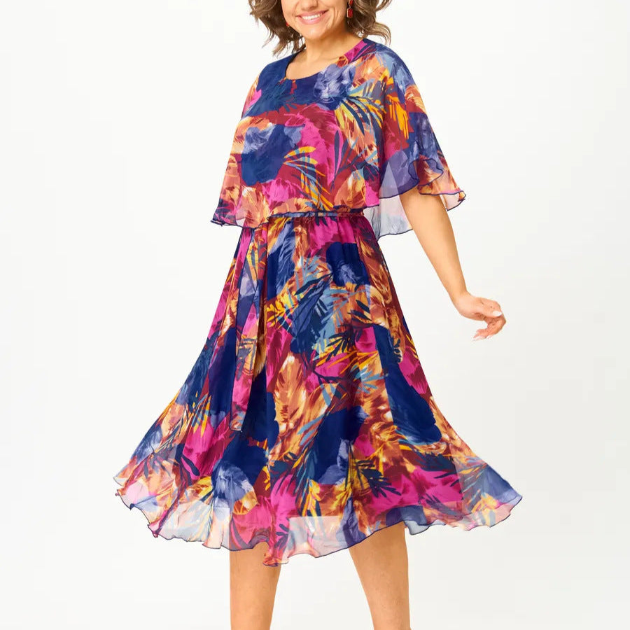 A flowing plus-size summer dress in a vibrant floral pattern with shades of blue and pink, featuring short sleeves. 0