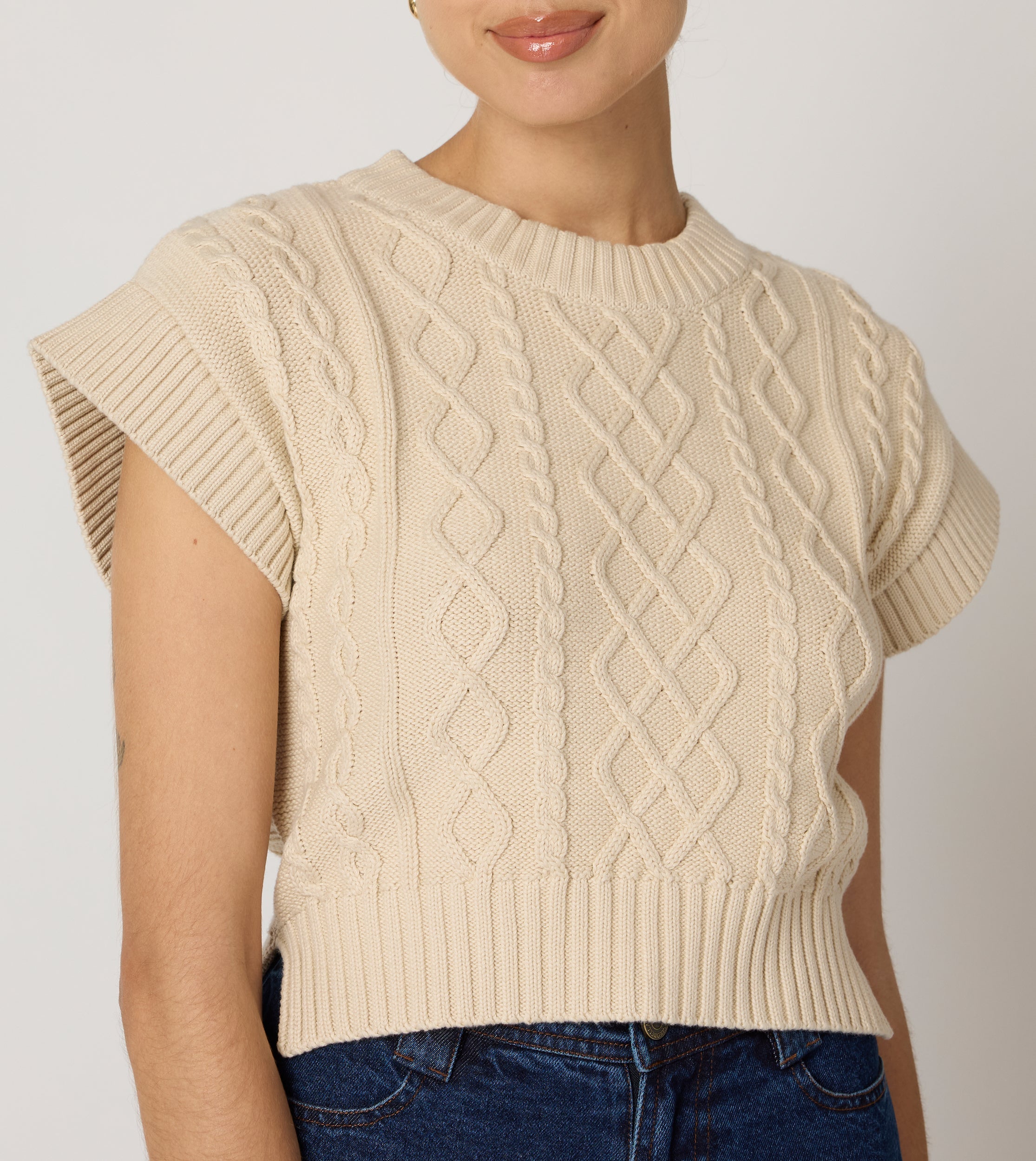 Cream cropped sweater vest in a cozy cable knit style, made from organic cotton for a soft, textured look. 0