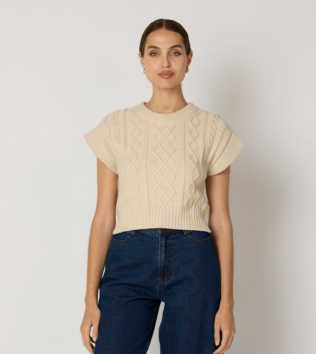 Cream cropped sweater vest in a cozy cable knit style, made from organic cotton for a soft, textured look. 2